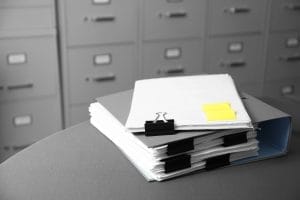 Una mano organizando documentos en una carpeta, con etiquetas y resaltadores, simbolizando la preparación y organización necesaria para una reclamación.